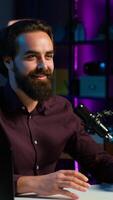 Vertical Content creator talking about himself while recording with production gear in home studio interior illuminated with RGB lights at night. Entertainer talking in professional microphone, camera A video