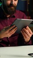 Vertical Tech specialist presenting tablet in entry level low budget price range to interested viewers, filming with smartphone on tripod. Man reviewing digital device, recording with mobile phone, camera A video