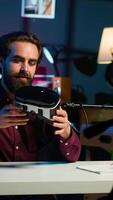 Vertical Close up shot of futuristic VR goggles held by man reviewing them for viewers. Internet star filming technology channel vlog for gadget enthusiasts, showcasing virtual reality headset, camera A video