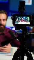 Vertical Focus on professional camera used by man in blurry background hosting online show in neon lit studio. Close up of high tech gear used by vlogger during streaming service broadcast, camera A video