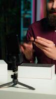 Vertical Entertainer presents smartphone from sponsoring brand, closely analyzing features. Content creator reviewing phone for tech enthusiasts watching his internet channel, inspecting materials, camera A video