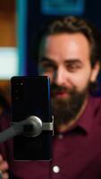 Vertical Focus on cellphone used by media star using on selfie stick to film vlog channel intro. Influencer greets viewers, presenting today topic, recording with mobile phone, camera A close up video