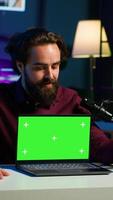 Vertical Man doing live broadcast talking to audience about recent news headlines, reading from chroma key laptop. Online show host presenting information from green screen notebook, camera A video