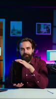 Vertical Entertaining man in studio films tablet review for tech enthusiasts. Viral media star hosts technology internet show, unboxing digital portable device, feeling impressed by thinness, camera B video