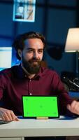 Vertical Smiling man in studio filming chroma key tablet review for tech enthusiasts. Cheerful online star hosts technology internet show, unboxing green screen digital portable device, camera A video