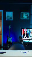 Vertical Happy influencer using microphone, arriving in dimly lit home studio interior, chatting with fans. Smiling man surrounded by podcast recording equipment in apartment starting stream, camera B video