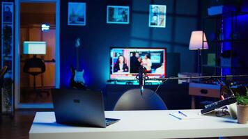 Panning shot of empty home studio interior illuminated with RGB lights at night, used for internet production. Apartment filled with content creation gear tech, TV running in background video