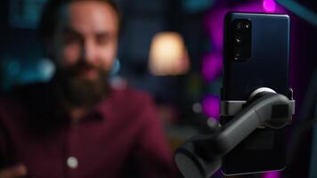 Focus on cellphone used by media star using on selfie stick to film vlog channel intro. Influencer greets viewers, presenting today topic, recording with mobile phone, camera B close up video