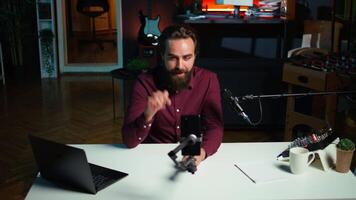 conteúdo O Criador falando dentro frente em celular em anexo para selfie bastão dentro estúdio, conversando com espectadores usando gravação microfone. homem usando telefone Câmera e profissional microfone para registro vlog, Câmera b video