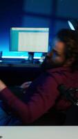 Vertical Childish man doing creative intro for vlog, using microphone to shoot . Energetic content creator spinning on chair while filming for vlogging channel with mic in home studio, camera A video