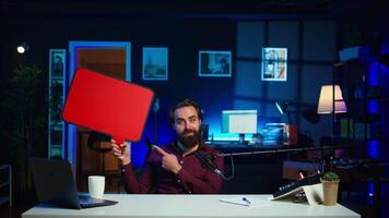 Man arriving in studio, filming sponsored content, holding empty copy space sign, following script, talking to audience. Internet star using cardboard bubble speech cutout to do marketing, camera B video