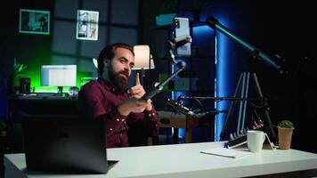 influenciador fazendo Paz placa dentro frente em celular em anexo para selfie bastão dentro estúdio, conversando com espectadores usando microfone. homem fazendo mão gesticulando, usando telefone e microfone para registro vlog, Câmera b video
