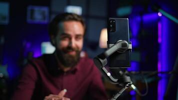 Focus on cellphone on selfie stick used by influencer in home studio recording live broadcast for online streaming platforms. Media star filming q and a session with mobile phone, camera B close up video