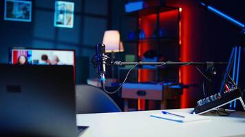 Close up of podcast microphone used to record videos for online show. Zoom in shot of streaming sound capturing and recording podcasting mic in empty living room with neon lights