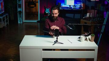 Man in studio endorsing laptop from brand sponsoring , filming with smartphone on tripod. Tech expert does influencer marketing by promoting notebook, recording with phone, camera B video