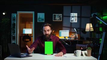 Tech specialist presenting chroma key tablet in entry level low budget price range to interested viewers, filming in studio. Viral content creator reviewing green screen digital device, camera B video