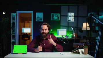 Tech specialist presenting mockup tablet to interested viewers, filming with professional mic. Man reviewing green screen digital device, recording with specialized equipment, camera B video