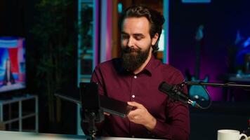 Man in studio endorsing laptop from brand sponsoring , filming with smartphone on tripod. Tech expert does influencer marketing by promoting notebook, recording with phone, camera A video