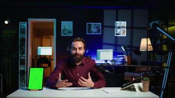 Happy influencer in studio filming chroma key tablet review for tech enthusiasts. Joyful media star hosts technology internet show, unboxing isolated screen digital portable device, camera B video