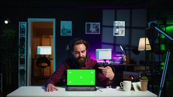 Man doing live broadcast talking to audience about recent news headlines, reading from chroma key laptop. Online show host presenting information from green screen notebook, camera B video