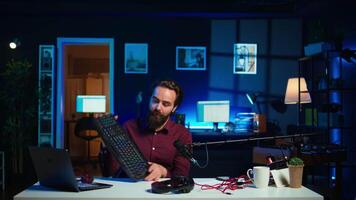 Influencer in studio reviewing gaming keyboard, mouse and headphones. Online show host filming electronics haul, presenting wired computer peripherals to viewers during live broadcast, camera B video