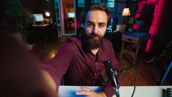 Happy influencer hosting online show in rgb lights studio, shooting vlog using selfie camera. POV of jolly media star talking during streaming service broadcast filmed with mobile phone video