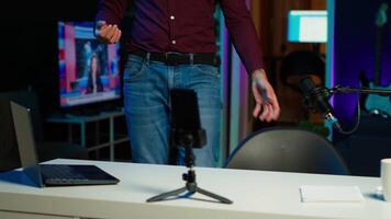 influenciador fala dentro frente em Smartphone em anexo para tripé e Alto qualidade microfone dentro estúdio, discutindo com espectadores. homem usando Móvel telefone e profissional engrenagem para registro social meios de comunicação , Câmera uma video
