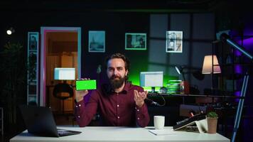 Man showing green screen cellphone, using it as empty copy space to showcase his online streaming channel logo. Media star does introductory using chroma key phone, camera B video