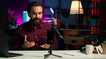 Media star talking in front on smartphone attached to tripod stabilizer in studio, discussing with viewers. Man using mobile phone to record in living room for social media, camera A video