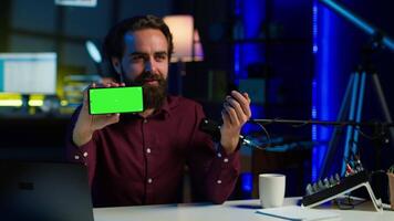 Man showing green screen cellphone, using it as empty copy space to showcase his online streaming channel logo. Media star does introductory using chroma key phone, camera A video