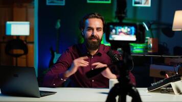 Upbeat content creator hosting online show in rgb lights studio, shooting vlog using professional microphone. Cheerful vlogger presenting informations during streaming service broadcast, camera A video