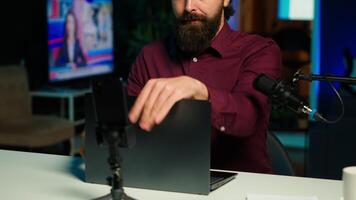 Tech expert assessing laptop performance, talking about components used inside, filming with smartphone. Entertainer reviewing notebook on technology internet channel, recording with phone, camera A video