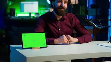 Tech specialist presenting mockup tablet to interested viewers, filming with professional mic. Man reviewing green screen digital device, recording with specialized equipment, camera A video