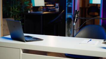 Laptop on desk in empty home production studio with podcast equipment technology recording sound for social media channel production. Notebook in live broadcasting space with neon lights video