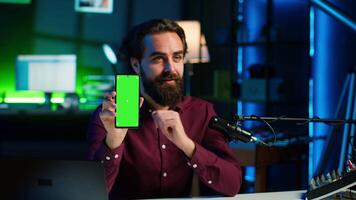 Upbeat tech specialist assessing mockup smartphone performance, feeling satisfied with high quality components used. Entertainer shooting isolated screen phone review for internet channel, camera A video