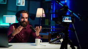 Joyful media star talking in professional microphone in studio at night, filming internet production. Smiling content creator uses quality mic to record vlog and speak to viewers, camera A video