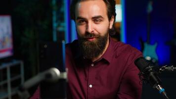 Happy influencer in home studio greeting audience, recording live broadcast using smartphone on selfie stick, close up. Man filming q and a session with mobile phone, answering questions, camera A video