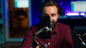 Focus on cellphone on selfie stick used by influencer in home studio recording live broadcast for online streaming platforms. Media star filming q and a session with mobile phone, camera A close up video