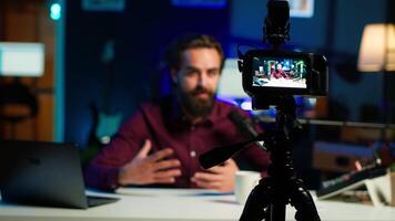 Focus on professional camera used by man in blurry background hosting online show in neon lit studio. Close up of high tech gear used by vlogger during streaming service broadcast, camera A video