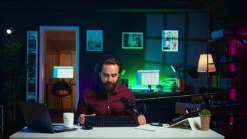 uomo le riprese per in linea canale nel debolmente illuminato casa studio, presentazione topo e tastiera per pubblico. soddisfare Creatore mostrando spettatori computer periferiche, dando onesto opinione, telecamera B video