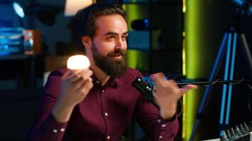 Smart light bulb used by tech specialist in studio to teach audience how to fix it, handheld camera shot. Focus on IoT home automation product held by media star, camera A video