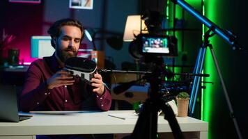 Close up shot of futuristic VR goggles held by man reviewing them for viewers. Internet star filming technology channel vlog for gadget enthusiasts, showcasing virtual reality headset, camera A video