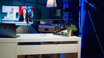 Panning shot of empty home studio illuminated with neon lights used for internet production. Living room filled with content creation equipment, TV animations running in background video