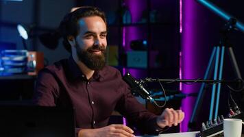 Content creator talking about himself while recording with production gear in home studio interior illuminated with RGB lights at night. Entertainer talking in professional microphone, camera A video