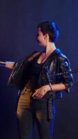 Vertical Rebellious rock performer protesting with a hush mute sign in studio, symbolizing no hate and anti bullying social messages. Rocker with leather jacket asking to be silent. Camera B. video