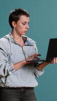 Vertical Casual woman browsing web on her laptop for freelance work in studio, remote network. Wireless computer user blogging on a new interface, trendy modern tech person. Camera B. video