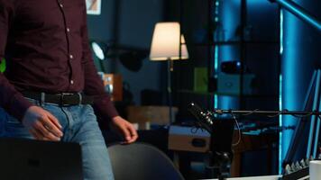 Content creator adjusting professional microphone in studio before starting vlog, recording with selfie camera. Man in neon lit home studio preparing equipment, filming with smartphone, camera A video