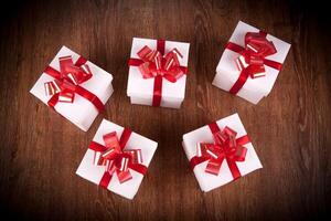 five white festive gift boxes with red bows on a wooden table photo