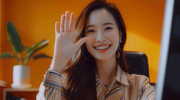 Smiling Asian Woman Waving During Call in Modern Office Setting photo