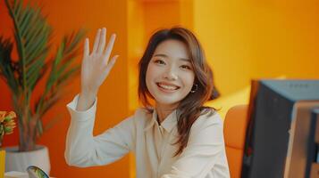 Smiling Asian Woman Waving During Call in Modern Office Setting photo